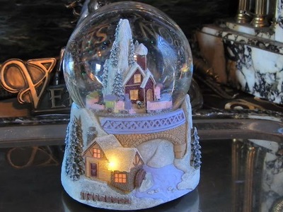 Kula świąteczna z pozytywką i oświetlonym domkiem w zimowej scenerii. Dookoła porusza się kolejka
